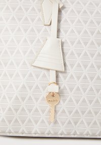 White handbag with a textured geometric pattern. Features a cream leather tag and a gold-toned keychain with “ALDO” engraved.