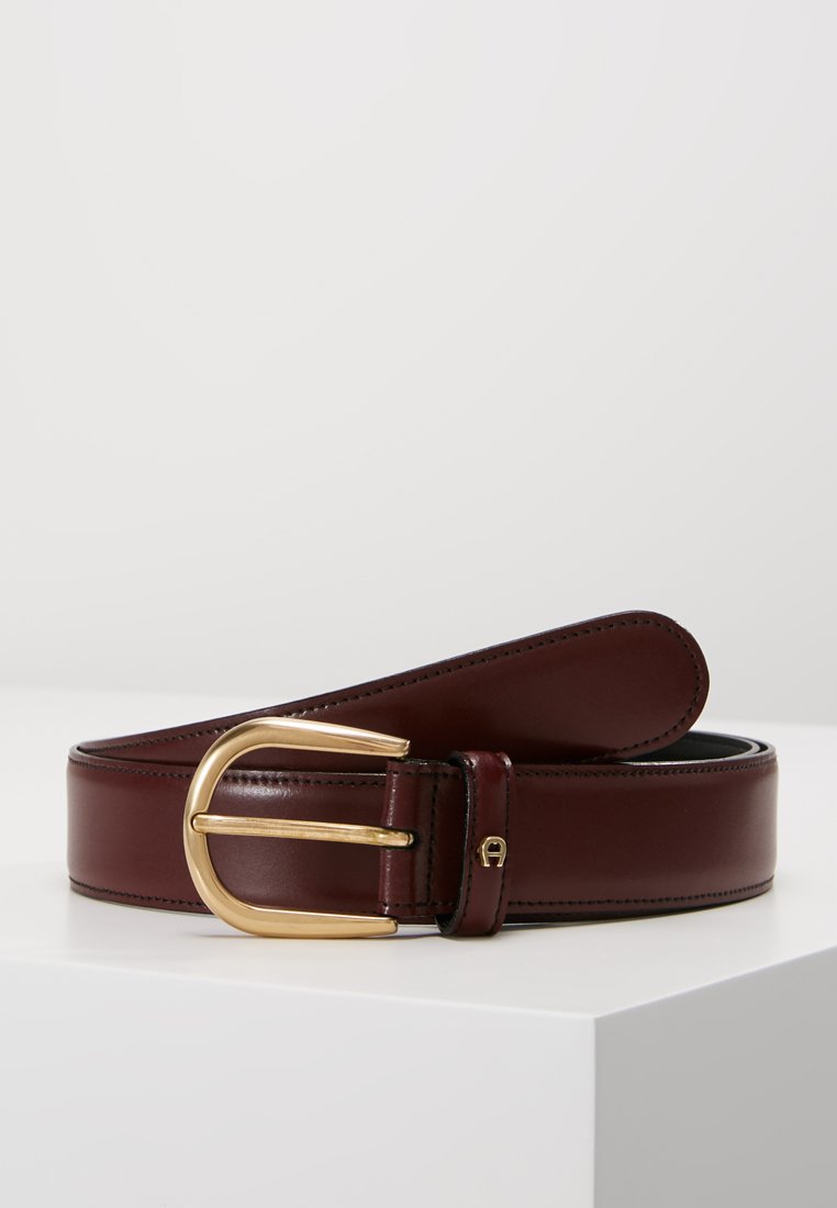 Bordeaux leren riem met een goudkleurige metalen gesp en stikdetails, met een gladde textuur en een klassiek ontwerp.