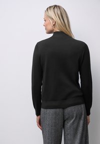 Zwart gebreid sweater met een hoge halslijn, lange mouwen en een aansluitende tailleband, gecombineerd met gestructureerde grijze houndstooth broek.