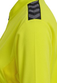 Fluoreszierendes gelbes Sporttrikot aus strukturiertem Stoff mit einem schwarzen gemusterten Akzent auf der Schulter.