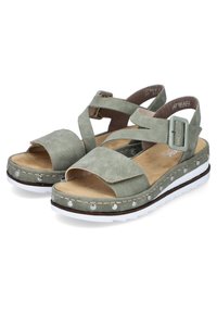 Sandales en daim vert avec une épaisse semelle blanche, dotées d'une bride de cheville, de brides croisées et de clous en argent autour du bord.