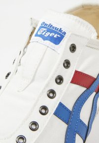 Sneaker bianca in tela con design a strisce blu e rosse, occhielli in metallo e logo blu di Onitsuka Tiger sulla linguetta.