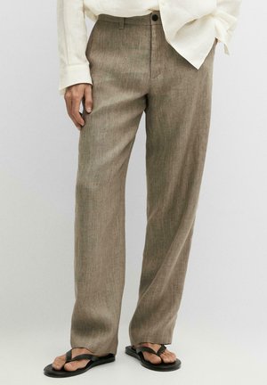 Beige Leinenhose getragen mit einem cremefarbenen Langarmhemd und schwarzen Flip-Flops, gezeigt an einer stehenden Person vor einem schlichten Hintergrund.