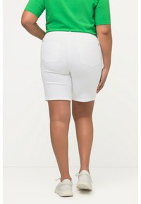 Pantalones cortos de denim blanco con un diseño ajustado, bolsillos traseros y una textura suave, combinados con una parte superior verde y zapatillas deportivas blancas.