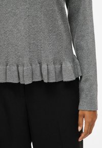 Szary sweter dzianinowy z teksturowanym, prążkowanym dolnym hemem oraz dopasowanymi rękawami, w połączeniu z czarnymi spodniami. Miękki materiał, casualowy design.
