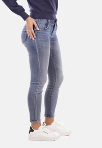 Jeans in denim leggero, blu chiaro, con una finitura sbiadita, cinque tasche e vita a media altezza. Abbinati a scarpe da ginnastica bianche e spesse.