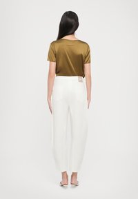 Olive green satin t-shirt with short sleeves, paired with white wide-leg trousers featuring back pockets and a brand tag on the waistband.