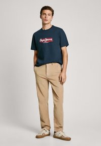Jūras zila kokvilnas T-kreklu ar sarkano "Pepe Jeans London" logotipu, apvienots ar bežām kordura biksēm un baltām kedām ar krāsainiem akcentiem.