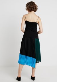 Svart ärmlös topp med en plisserad flerfärgad kjol, som har sektioner i svart, teal och blått, accentuerad med en insydd midjedesign.