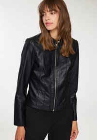 Giubbotto di pelle nera con design attillato, chiusura con zip e superficie liscia. Presenta cuciture a pannello e colletto rialzato.