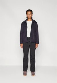 Casaco de lã polar azul-marinho com capuz, combinado com calças pretas e sapatilhas castanhas. O casaco apresenta um fecho de correr e bolsos laterais.