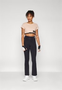 Lys rosa cropped t-skjorte med svart "NE" trykk, kombinert med svarte tettsittende leggings, hvite treningssko og fingerløse hansker.