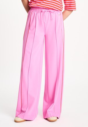 Persoon draagt loszittende felroze broek met zijstrepen, elastische taille, gecombineerd met beige schoenen en een rood-wit gestreepte top.