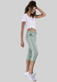 Pantalones de chándal de color verde claro, cortos, con rayas blancas en los laterales y cinturilla elástica. Combinados con una camiseta blanca anudada y zapatillas deportivas.