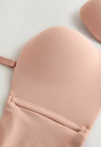 Polstret bh i blødt pink stof med glat tekstur og justerbare stropper. Har formede skåle og syningsdetaljer langs båndet.