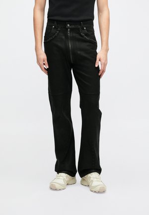 Calças de denim pretas com fecho de correr frontal, fecho de botão e acabamentos em bainha crua. Apresentam um corte de perna reta e detalhes de costura discretos.