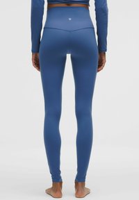 Vysoké modré legíny vyrobené z hladkého, elastického materiálu s priliehavým strihom, s diskrétnym logom na zadnej strane a bez švov.