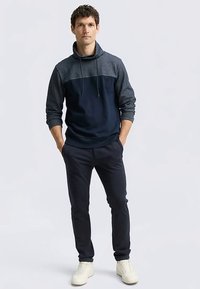 Felpa con cappuccio bicolore blu navy e grigio, maniche lunghe, collo con coulisse e tessuto a contrasto. Abbinata a pantaloni scuri e sneakers bianche.