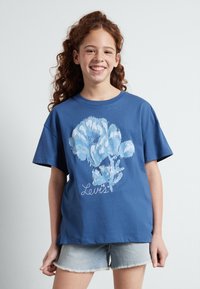Camiseta de algodón azul con mangas cortas y un corte relajado. Presenta un gran gráfico floral en azul claro y el texto "Levi's" en blanco.