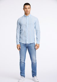 Jasnoniebieska koszula w białe paski, z guzikiem, slim fit, z długimi rękawami i kołnierzykiem, zestawiona z jasnoniebieskimi dżinsami i białymi trampkami.