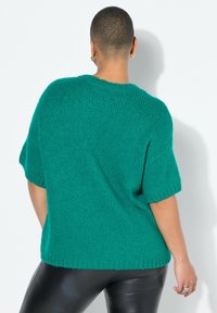 Tyrkis strikket sweater med kortærmer, ribbet kant og en afslappet pasform. Båret over sorte faux læderbukser, der fremhæver teksturkontrasten.