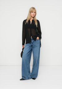 Cămașă neagră transparentă cu nasturi, blugi largi de denim albastru deschis, geantă neagră și pantofi ascuțiți negri. Țesătură netedă și croială lejeră.