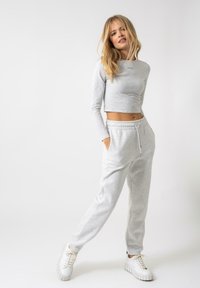 Lysegrå kortermet topp med lange ermer og diskret merkevare, sammen med matchende joggebukser med elastisk midje og sidelommer. Hvite joggesko.