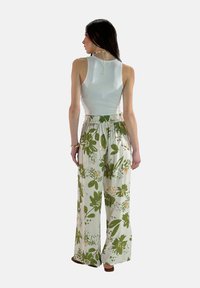 Lichtblauw mouwloos topje gecombineerd met losse, witte broek met een groen bloemenpatroon en elastische taille.