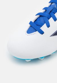 Close-up of a white football boot with blue laces and cleats on a light background.