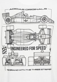 Balti marškinėliai, kuriuose pavaizduoti lenktyniniai automobiliai juodomis linijomis, pažymėti užrašais „ADIDAS ORIGINALS“ ir „ENGINEERED FOR SPEED“.