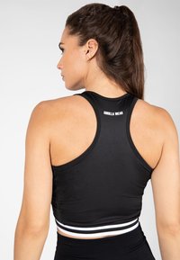 Černý sportovní crop top s designem na závodní záda, který má bílé a šedé pruhované akcenty na lemu, vyrobený z hladkého, elastického materiálu.