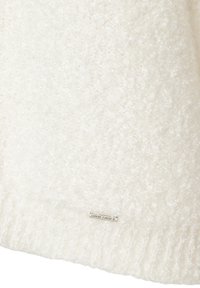 Weißer flauschiger Pullover mit einer weichen Textur, ribbelt am Saum und hat ein kleines Metalletikett am unteren Rand.