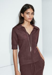 Bordeaux strikbluse med korte ærmer, en V-udskæring og en krave. Sammen med matchende bukser, der har en glat tekstur og minimale detaljer.