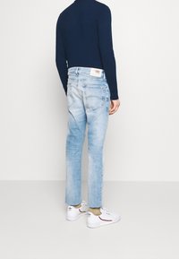 Ljusblå denimjeans med rak skärning, slitna texturer och en Tommy Jeans-lapp på bakfickan, matchat med vita sneakers.