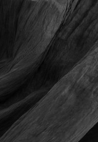 Tissu noir texturé avec un aspect froissé, présentant des plis doux et fluides qui créent de la profondeur et une variation dans la réflexion de la lumière.