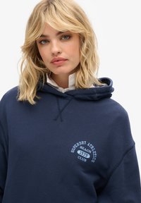 Felpa blu navy con cappuccio regolabile e logo sul petto anteriore. Realizzata in tessuto morbido, ha un fit rilassato e polsini a costine.