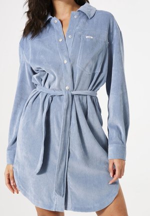Lichtblauwe corduroy overhemdjurk met lange mouwen, een knoopsluiting aan de voorkant, een ceintuur en een borstzak; licht gebogen zoom.