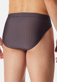 Marineblaue Schwimmslips mit dünnen orangen senkrechten Streifen. Hergestellt aus glattem, dehnbarem Material, mit einem niedrigen Bund und sauberen Nähten.