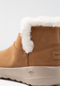 Stivaletto in suede marrone con un colletto morbido bianco, suola in gomma leggera e dettagli cuciti lungo il bordo superiore.