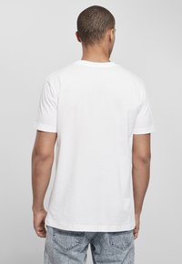 Balta medvilnė t-shirt marškiniai su trumpomis rankovėmis ir apvalia iškirpte, pasižymintys lygiu paviršiumi ir laisvu siluetu, matomi iš nugaros.