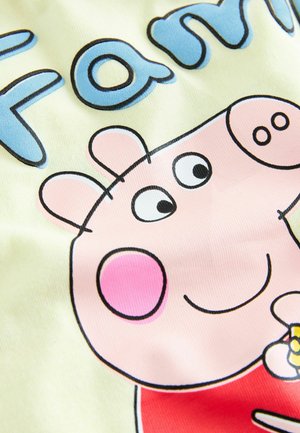 Gelbes Fabric mit einem Cartoon-Schwein Charakter, der ein pinkes Gesicht, rosige Wangen und ein rotes Shirt hat. Blauer Text mit der Aufschrift "Familie" steht über dem Charakter.