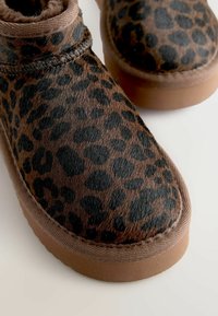 Brune leopardprint ankelstøvler lavet af blødt pels, der har sorte pletter, en syet søm og en slidstærk brun gummisål.