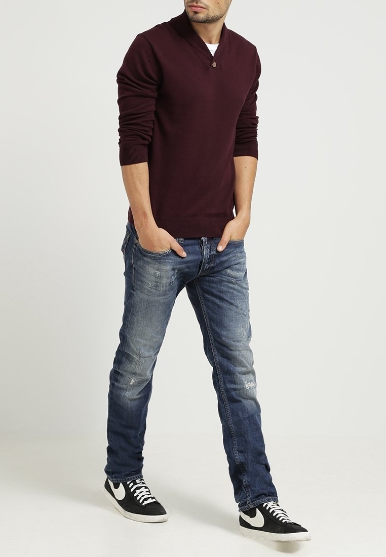 Camisa henley de manga larga color burdeos con cuello abotonado, combinada con jeans azules desgastados y zapatillas en blanco y negro.