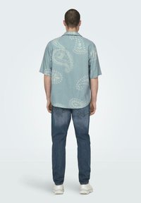 Kurzärmeliges, hellblaues Hemd mit Paisleymuster, kombiniert mit dunkelblauen Jeans. Das Hemd hat einen lockeren Schnitt und einen Kragen.