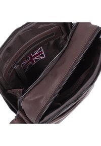 Interno di una borsa in pelle marrone con molteplici scomparti, dotata di una tasca con zip e un'etichetta con la bandiera britannica. Texture liscia e design pratico.