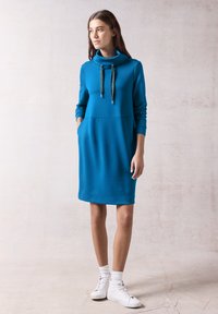 Cyan sininen college-mekko, jossa on korkea kauluri, pitkät hihat, etutaskut ja nyörikoristeet. Sujuva kangas ja rento istuvuus.