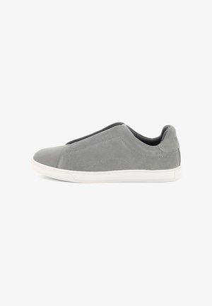Sneaker slip-on grigio in suede con suola in gomma bianca e dettagli minimi di cuciture, fotografata su sfondo bianco.