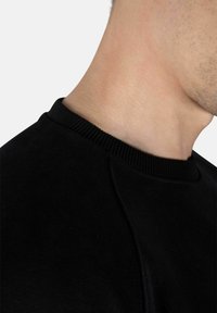 Sudadera negra con cuello acanalado, tejido suave y mangas raglán, que resalta una textura suave y un detalle de costura limpia.