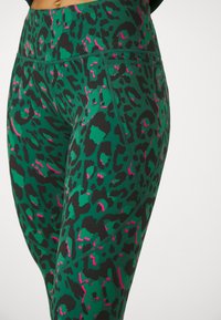 Gröna leggings med ett svart och rosa leopardmönster, tillverkade av ett mjukt, stretchigt material. Har en hög midja och en strömlinjeformad design.