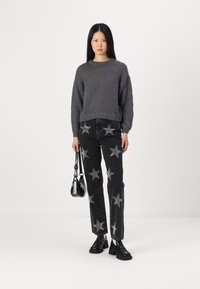 Grå strikket genser, svarte jeans med sølvstjerne-mønster, svart skulderveske, kraftige svarte sko. Modell står mot en hvit bakgrunn.